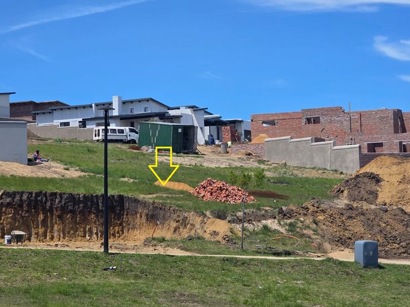 A vacant residential plot featuring sloped terrain and existing earthworks, situated within a developing neighborhood with surrounding construction activity.