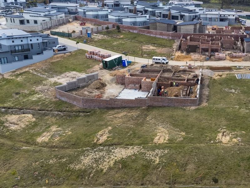 Aerial view of a residential vacant land plot showing ongoing construction of brick foundations and perimeter walls within a developing estate.