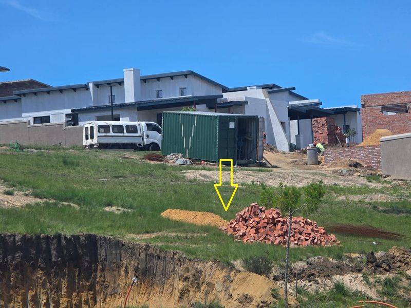 A view of a vacant residential plot under development, featuring uneven terrain, excavation work, and surrounding construction activity.