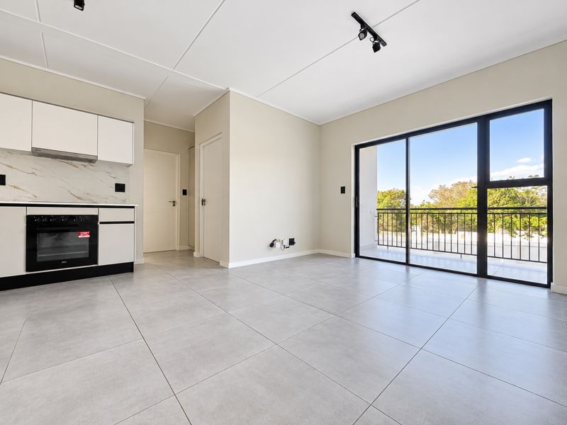 Modern open-plan living area featuring a sleek kitchen with built-in oven, tiled floors, and large sliding doors leading to a private balcony.