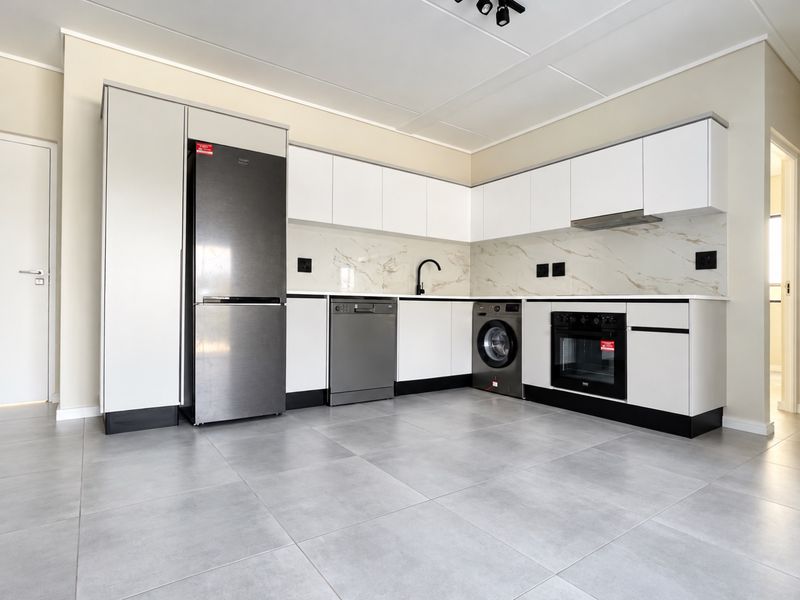 Modern kitchen featuring sleek white cabinetry, marble-look splashback, integrated oven, extractor fan, and neutral tiled flooring in a clean, contemporary layout.