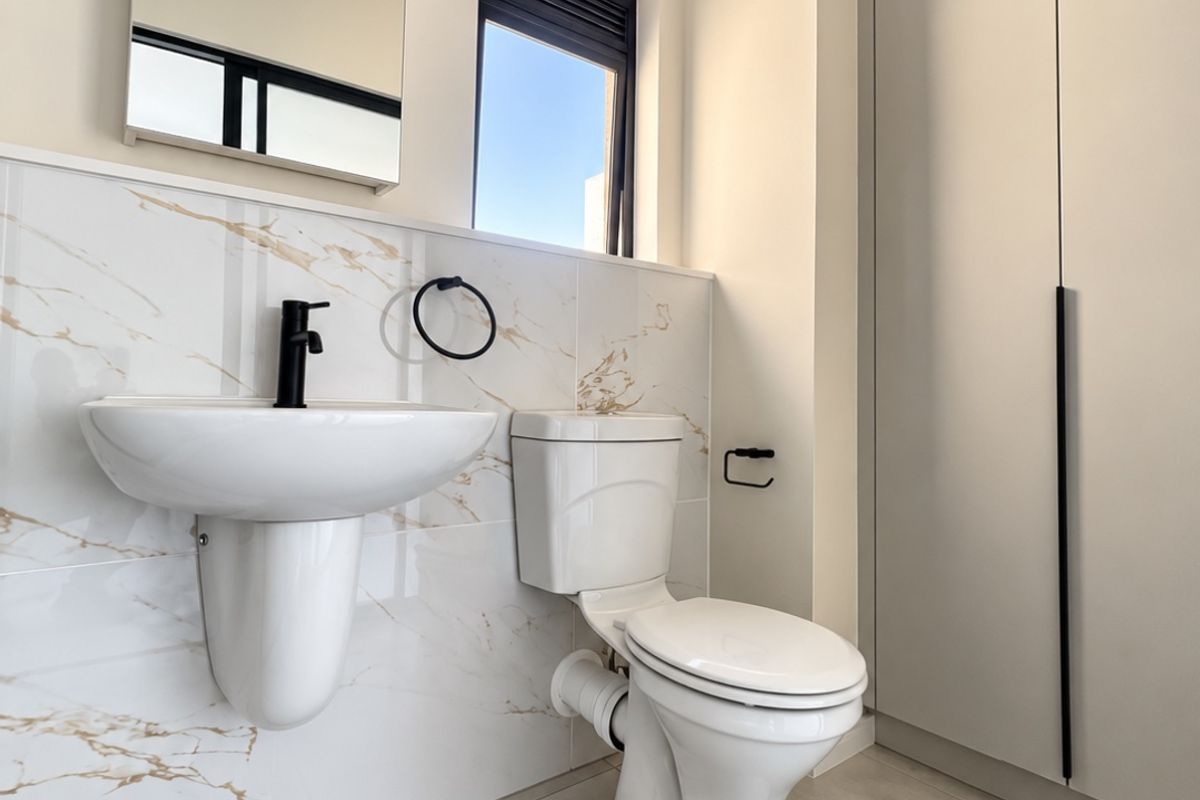 Modern bathroom featuring a wall-mounted basin, toilet, marble-look wall tiles, and a built-in cupboard with sleek black hardware.