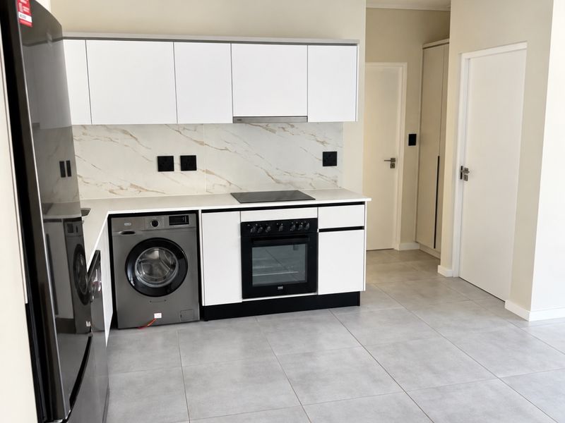 Modern kitchen featuring white cabinetry, marble-look splashback, integrated oven and hob, and neutral tiled flooring in a clean, well-maintained space.