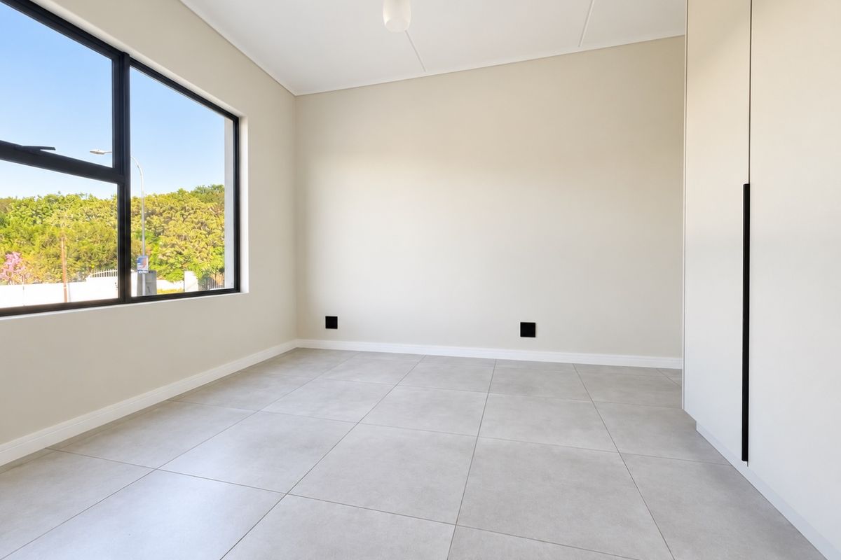 A bright, modern, and empty bedroom featuring neutral tiled flooring, built-in cupboards, and a large window providing ample natural light.