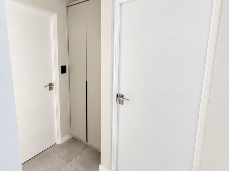 A clean and modern hallway featuring neutral tiled flooring, built-in storage cabinetry, and contemporary internal doors.