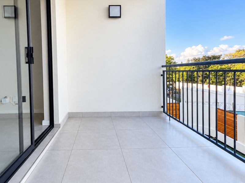 A clean, modern balcony featuring neutral floor tiles, a sleek black metal balustrade, and a sliding glass door providing access to the interior.