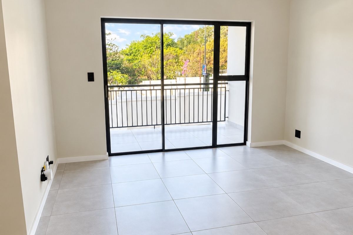 A bright, modern, and empty living area featuring large format floor tiles, track lighting, and a black aluminium sliding door leading to a balcony.