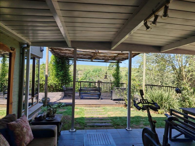A spacious covered patio featuring tiled flooring and a seamless transition to an outdoor timber deck with scenic garden and landscape views.