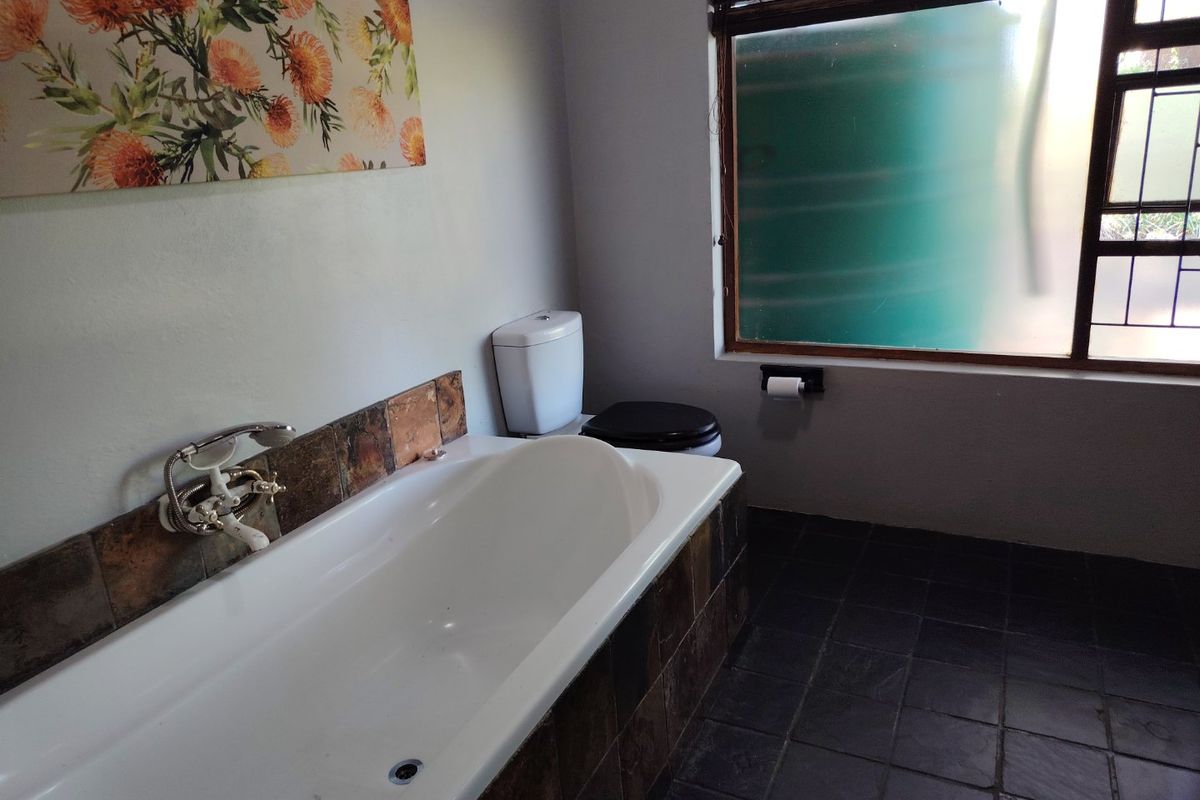 A functional bathroom featuring a built-in bathtub with tiled surround, slate flooring, and a window with security bars.