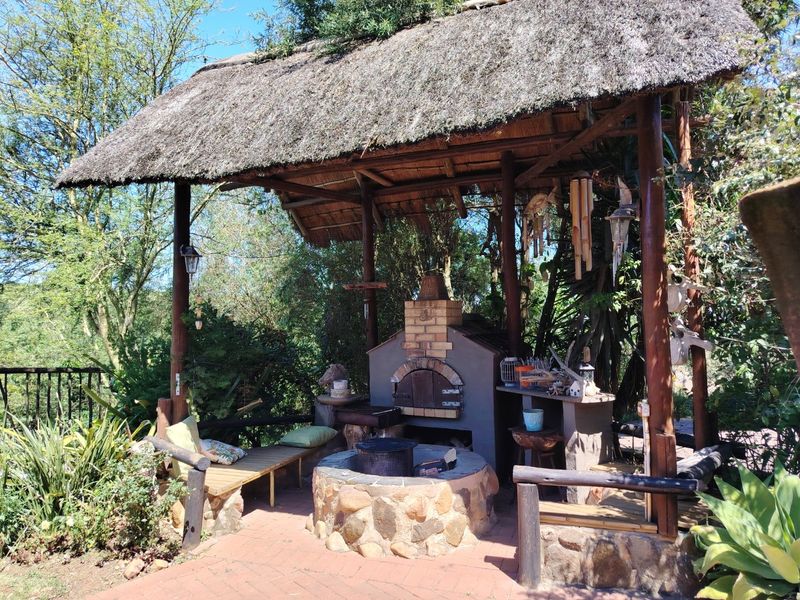 Outdoor entertainment area featuring a thatched roof, built-in brick pizza oven, and a stone-clad fire pit set on brick paving.