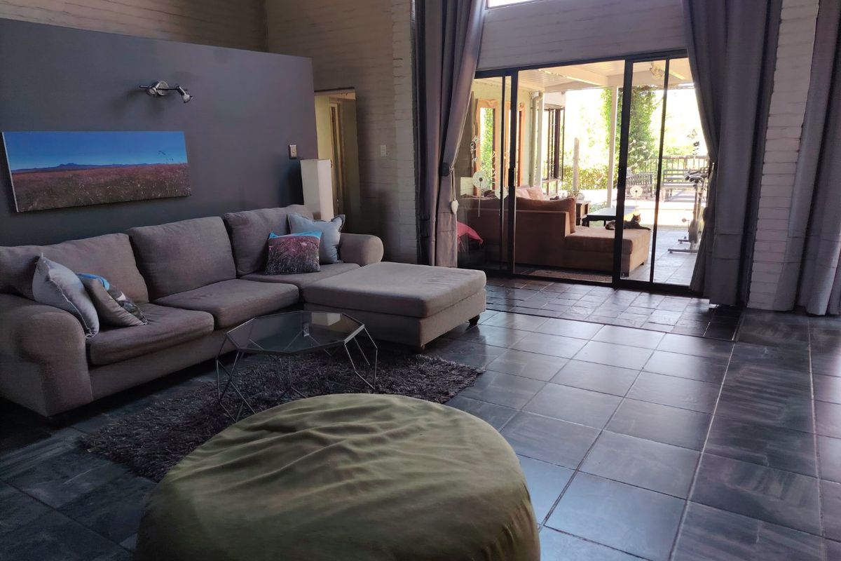 Spacious living room featuring double volume ceilings, exposed brick walls, and large sliding glass doors that open onto an outdoor patio area.