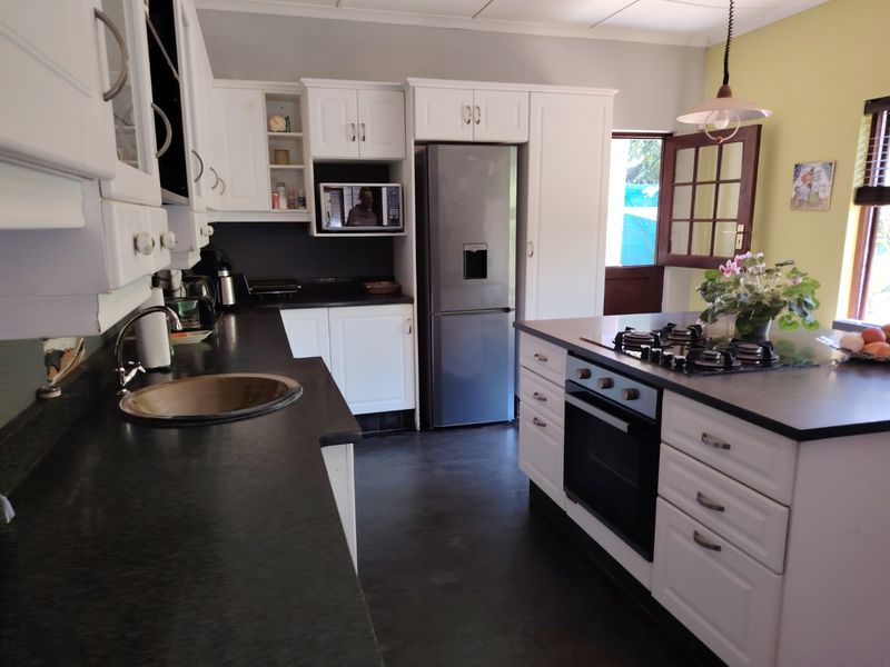 A functional kitchen featuring white cabinetry, dark countertops, a central island with a built-in oven and gas hob, and direct access to the outdoors.