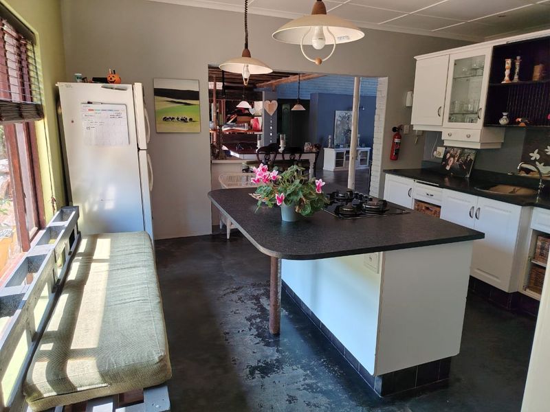 A functional kitchen featuring a central island with a gas hob, white cabinetry, and durable concrete flooring, opening into an adjacent living space.