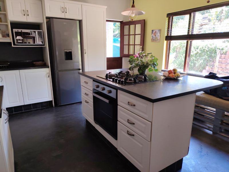 A functional kitchen featuring a central island with a built-in gas hob and oven, complemented by white cabinetry and dark countertops.
