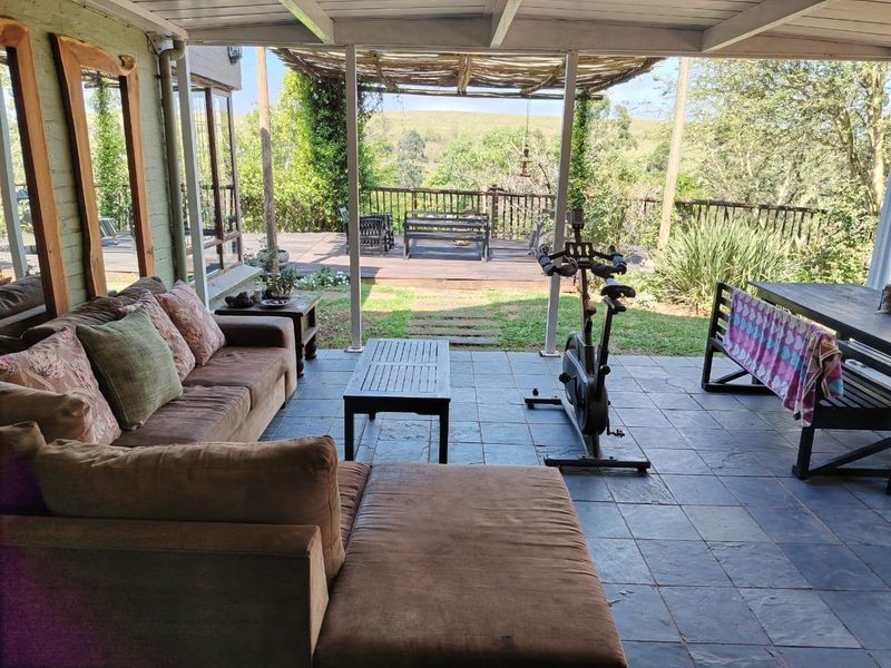 Spacious covered patio featuring slate tile flooring, transitioning to an open timber deck with scenic garden and landscape views.
