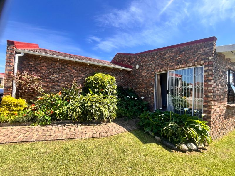 A well-maintained rear exterior view of a face brick townhouse featuring a paved walkway, established garden, and a sliding glass door with security gate.