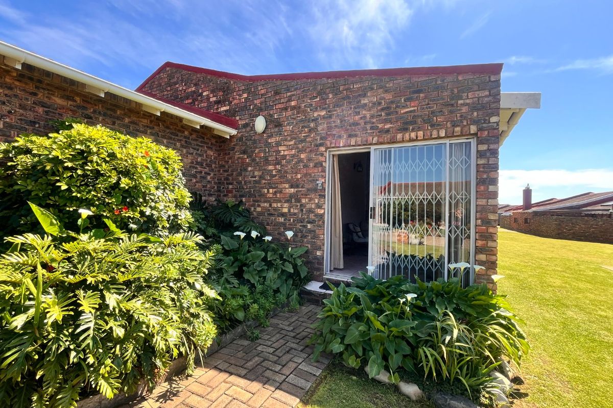 Rear exterior view of the townhouse featuring a face brick facade, paved walkway, and a sliding glass door with a security gate.