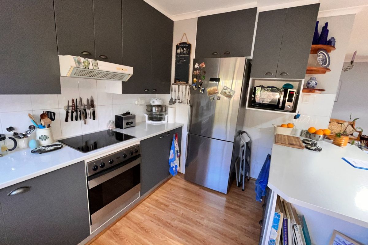 Modern kitchen featuring dark grey cabinetry, integrated appliances including an oven and cooktop, tiled backsplash, and a functional breakfast bar area.