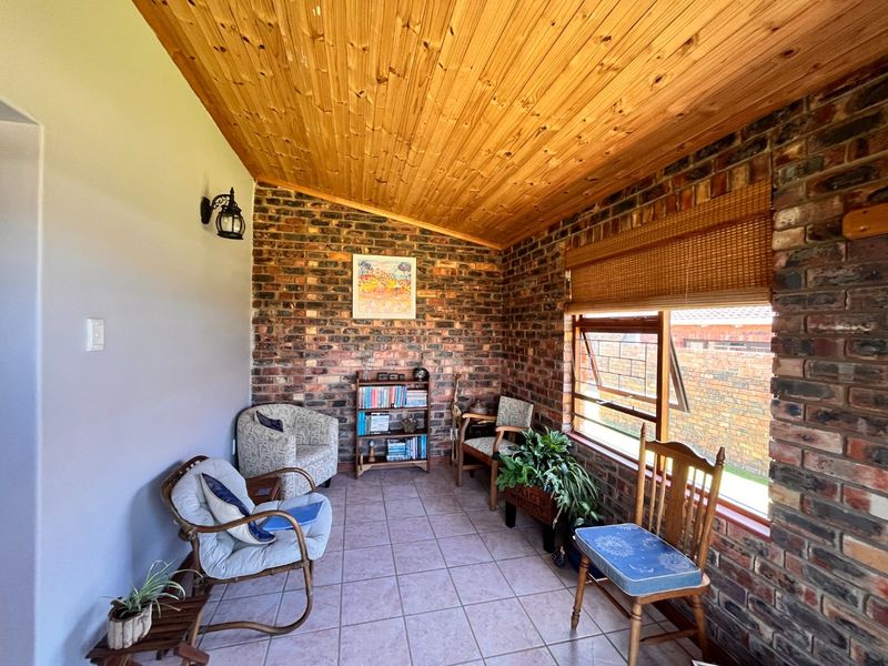 A sunroom or enclosed patio featuring exposed brick walls, a warm timber ceiling, and tiled flooring, offering a cozy space with natural light.