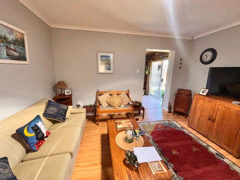 A comfortable living room featuring laminate flooring and neutral wall tones, with direct access to an adjacent patio area through a security gate.