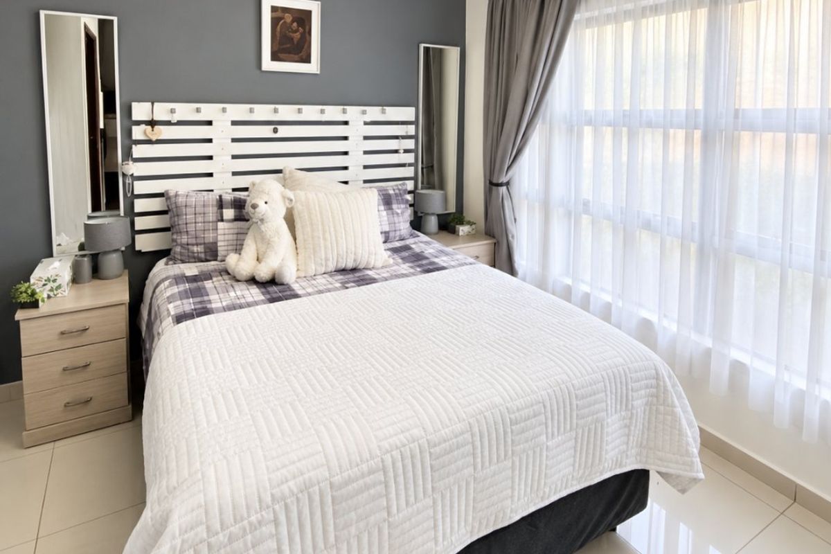 A well-maintained bedroom featuring neutral tiled flooring, crown molding, and a large window allowing for ample natural light.