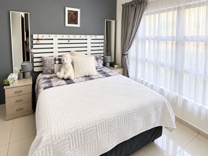 A well-maintained bedroom featuring neutral tiled flooring, crown molding, and a large window allowing for ample natural light.