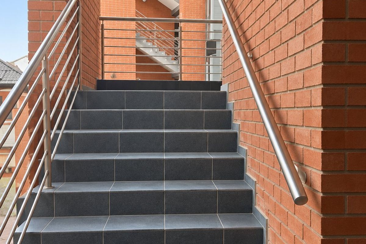 An exterior staircase featuring modern dark tiling, stainless steel handrails, and exposed red brick walls leading to an upper level.