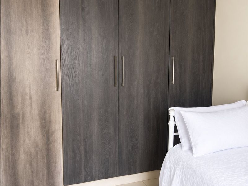 A bedroom featuring modern dark wood-grain built-in cupboards, neutral tiled flooring, and classic crown molding.