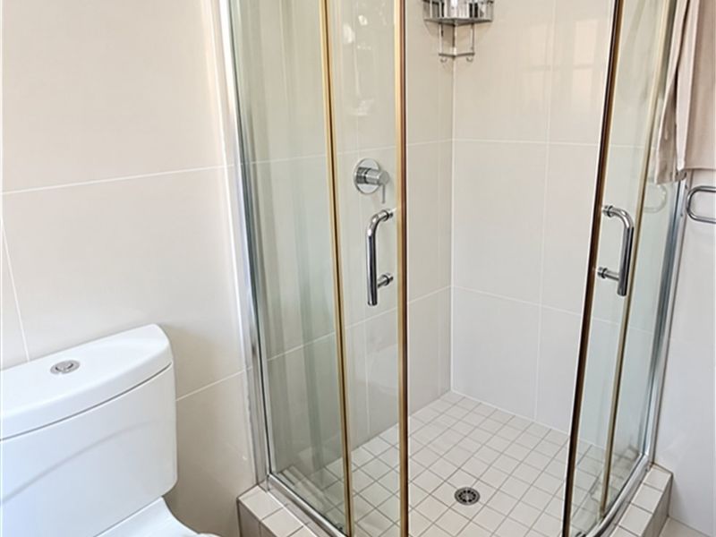 A clean and modern bathroom featuring a corner shower enclosure with a rainfall shower head and a dual flush toilet.