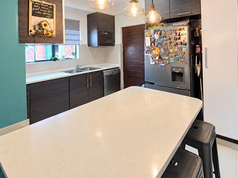 Modern kitchen featuring dark wood cabinetry, a stone-topped island, integrated dishwasher, and stylish pendant lighting, creating a functional and contemporary cooking space.