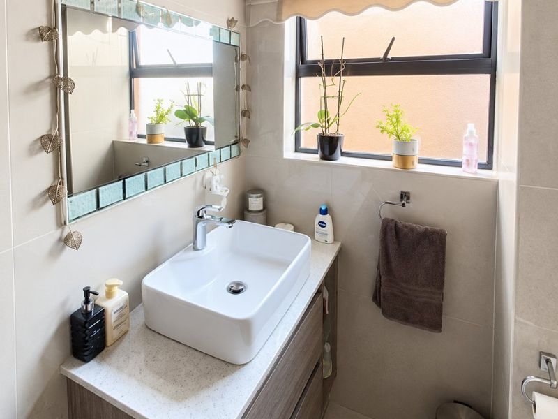 A modern bathroom featuring a sleek vanity cabinet with a countertop basin, neutral wall tiling, and a window with a roller blind.