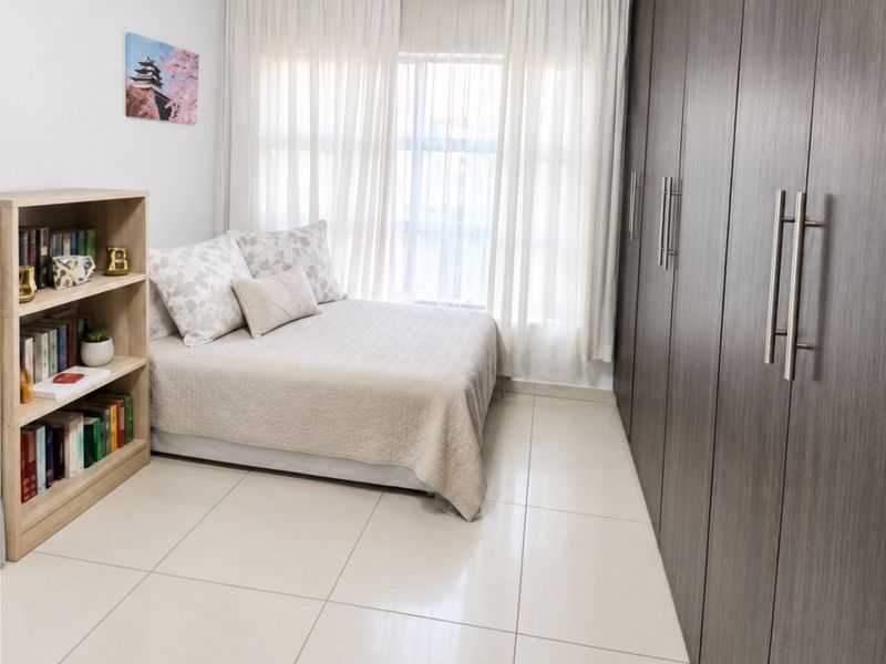 A well-maintained bedroom featuring large built-in cupboards, neutral tiled flooring, and elegant cornice detailing, providing a clean and functional living space.