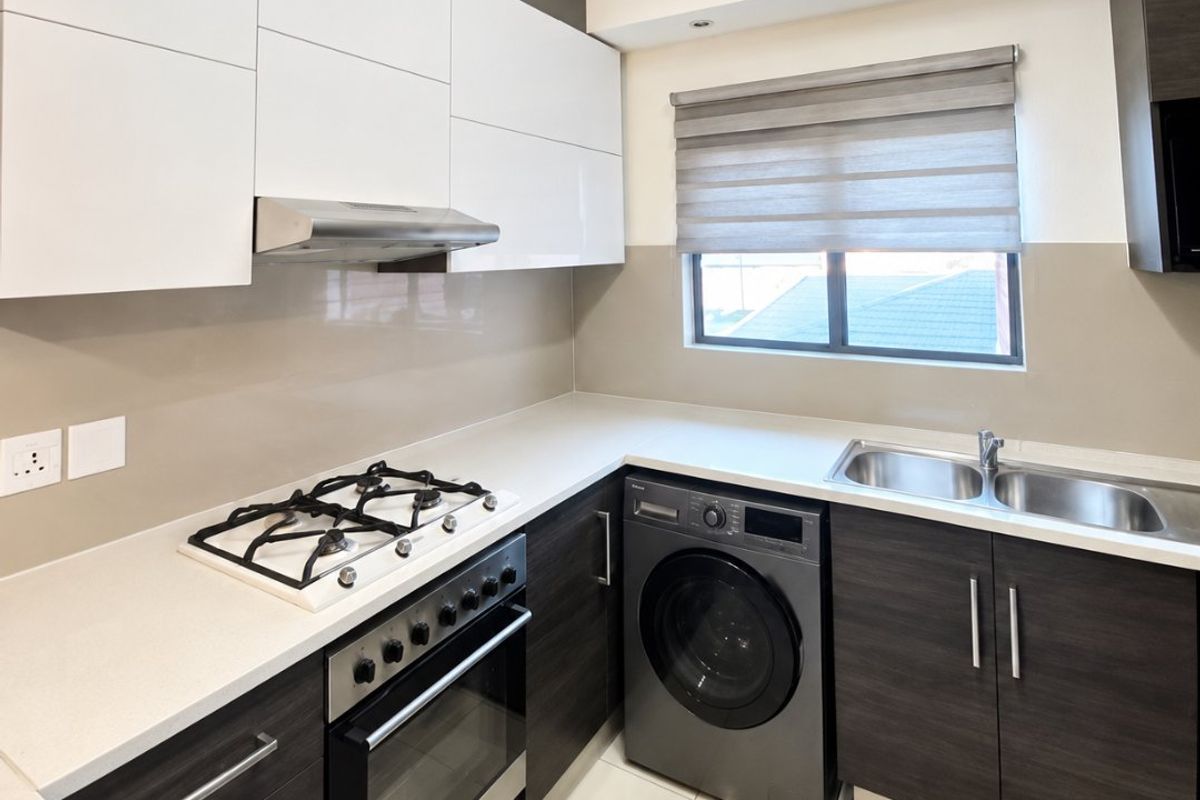 Modern kitchen featuring high-gloss white upper cabinets, dark wood-grain lower cabinetry, stone countertops, gas hob, built-in oven, and integrated laundry appliance space.