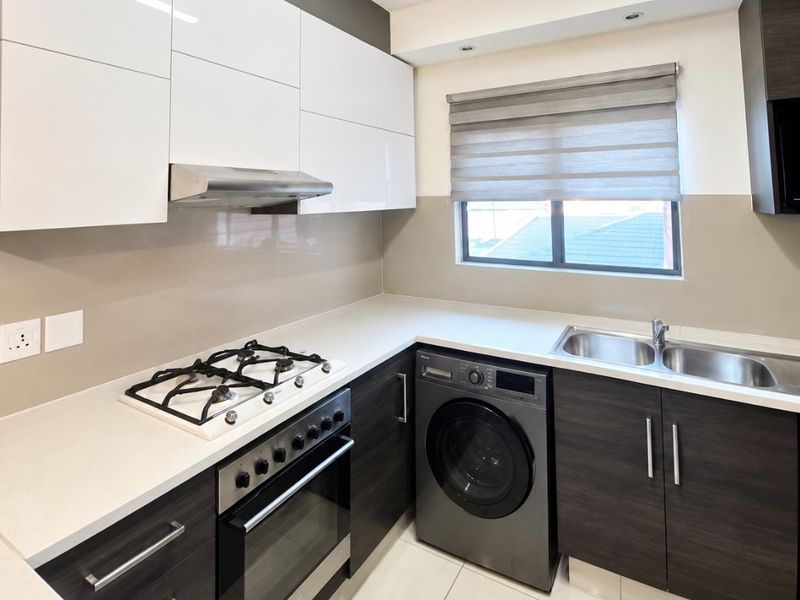 Modern kitchen featuring high-gloss white upper cabinets, dark wood-grain lower cabinetry, stone countertops, gas hob, built-in oven, and integrated laundry appliance space.