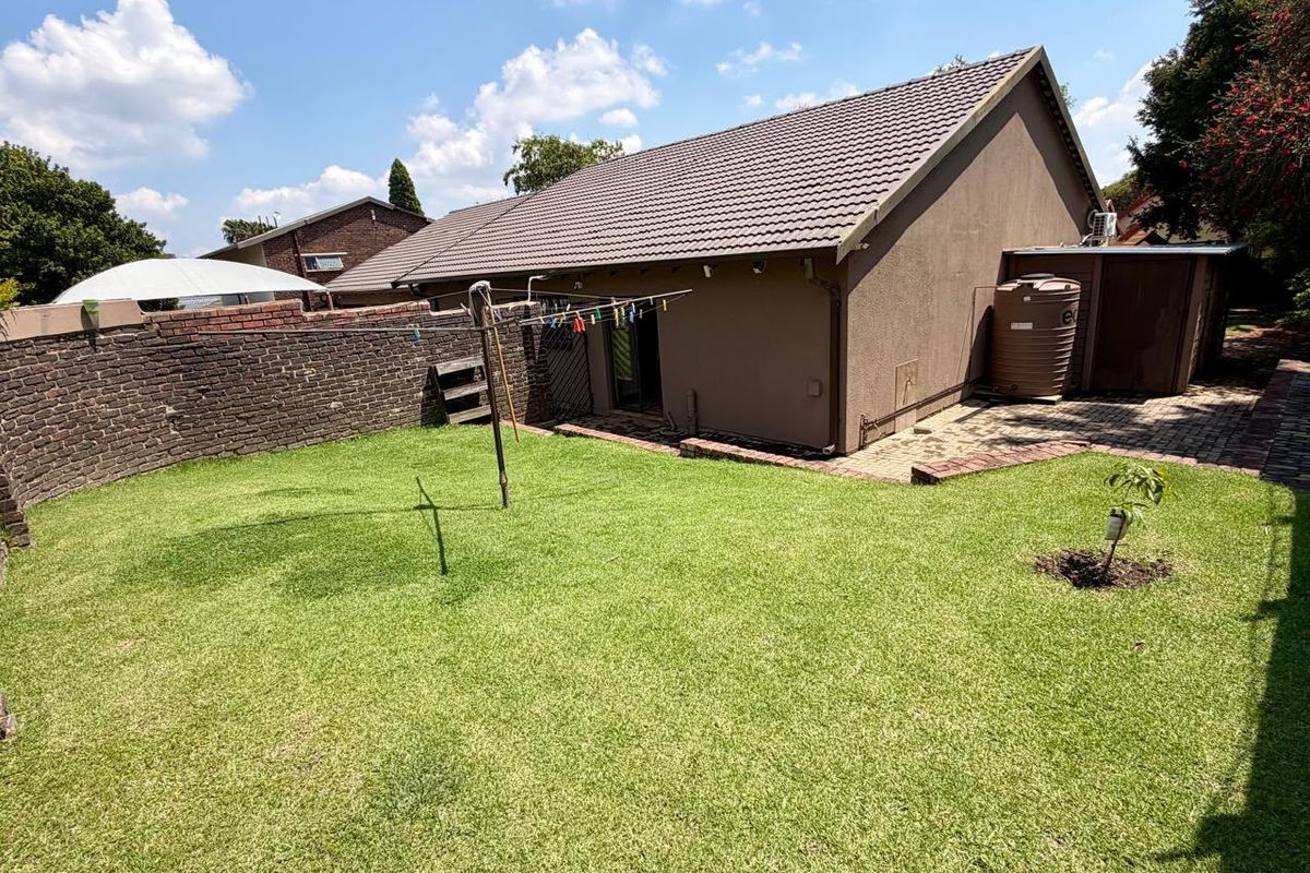A rear exterior view of the property featuring a well-maintained lawn, paved patio area, brick boundary wall, and a water storage tank.