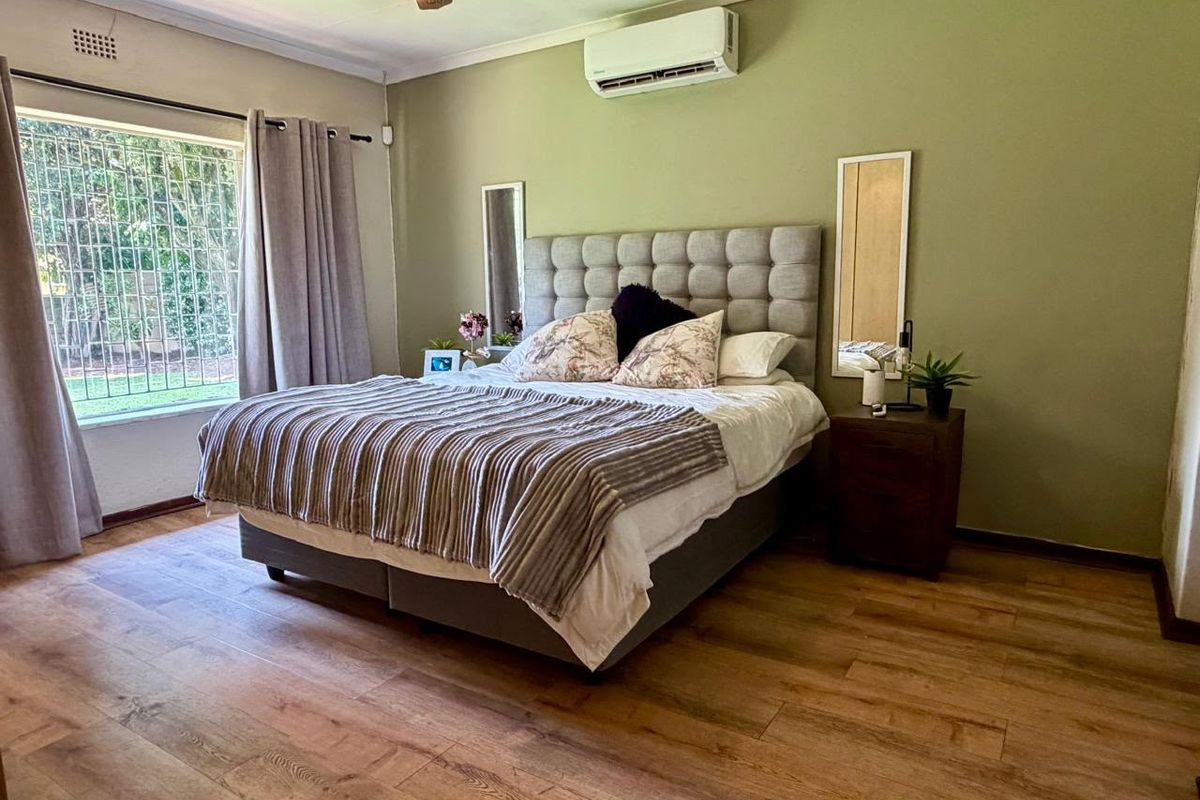 A well-maintained bedroom featuring laminate flooring, a split-system air conditioner, and large windows with security bars for added safety.