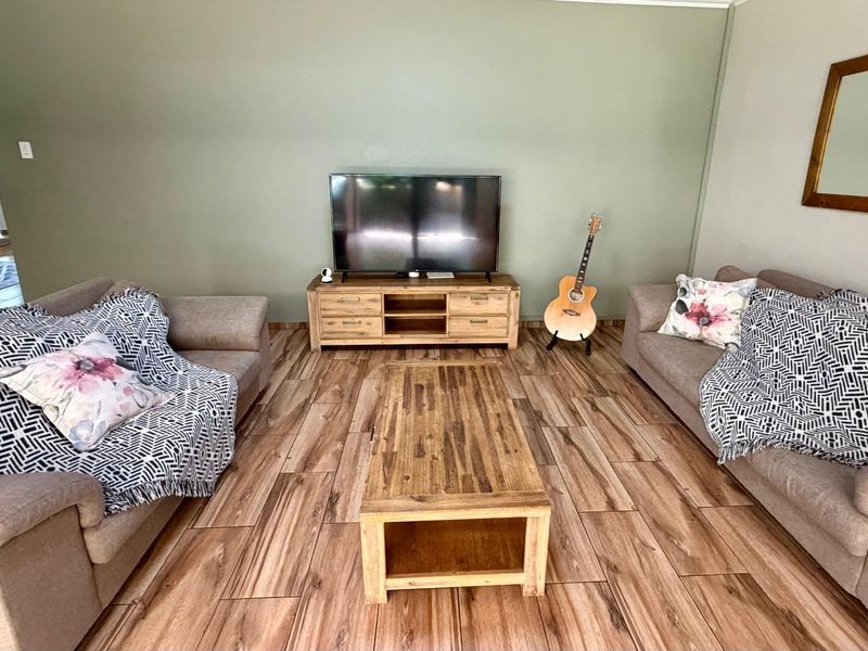 A comfortable living room featuring wood-look tile flooring and a neutral green accent wall, providing a warm and inviting atmosphere.