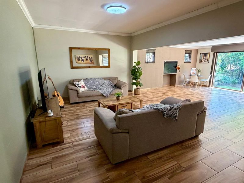 Spacious open-plan living area featuring wood-look tile flooring, a built-in fireplace, and large sliding glass doors providing access to the garden.
