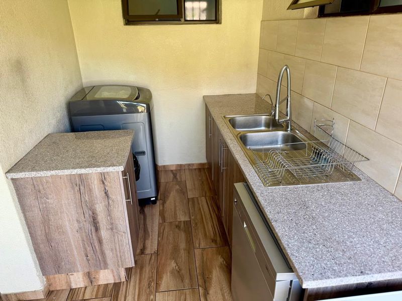 A functional laundry area featuring granite countertops, a double basin sink with a modern faucet, and wood-look floor tiles.