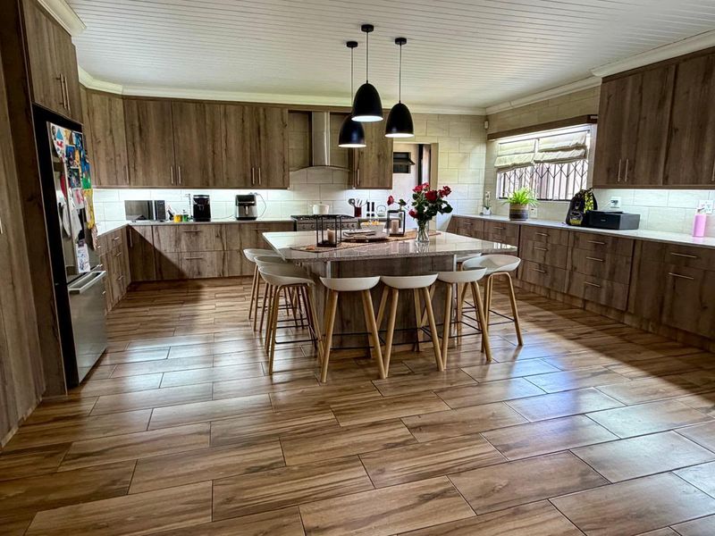 Spacious modern kitchen featuring wood-look cabinetry, stone countertops, a large central island, and integrated lighting, finished with durable tiled flooring.