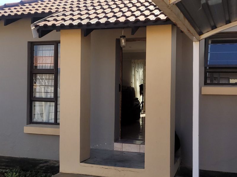 Front exterior view of the townhouse featuring a paved driveway, covered carport, and a covered entrance porch with tiled roofing.
