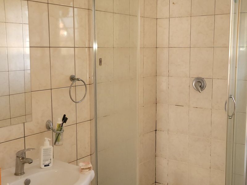 A functional bathroom featuring a shower enclosure with glass doors, a vanity cabinet with a basin, and tiled walls and flooring.