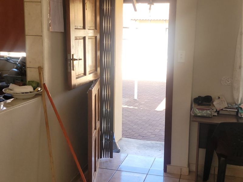 An interior entry area featuring tiled flooring, a wooden door with a security gate, and crown molding, leading out to a paved exterior space.
