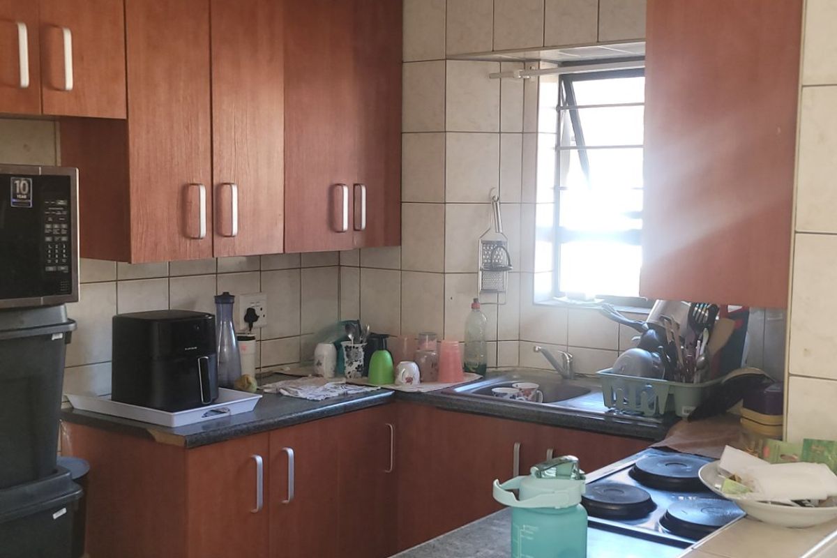 Compact kitchen featuring wooden cabinetry, tiled backsplash, laminate countertops, and an integrated electric hob, offering a functional layout with natural light.