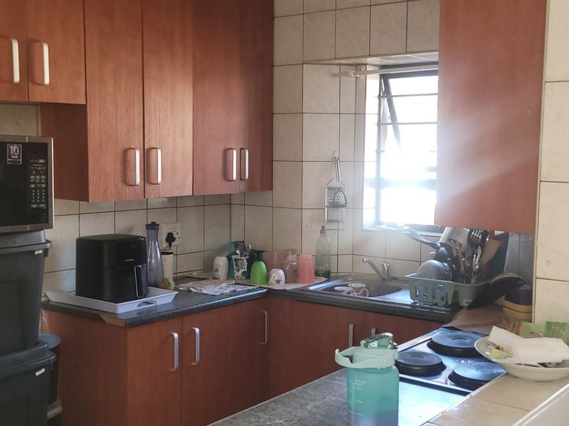 Compact kitchen featuring wooden cabinetry, tiled backsplash, laminate countertops, and an integrated electric hob, offering a functional layout with natural light.