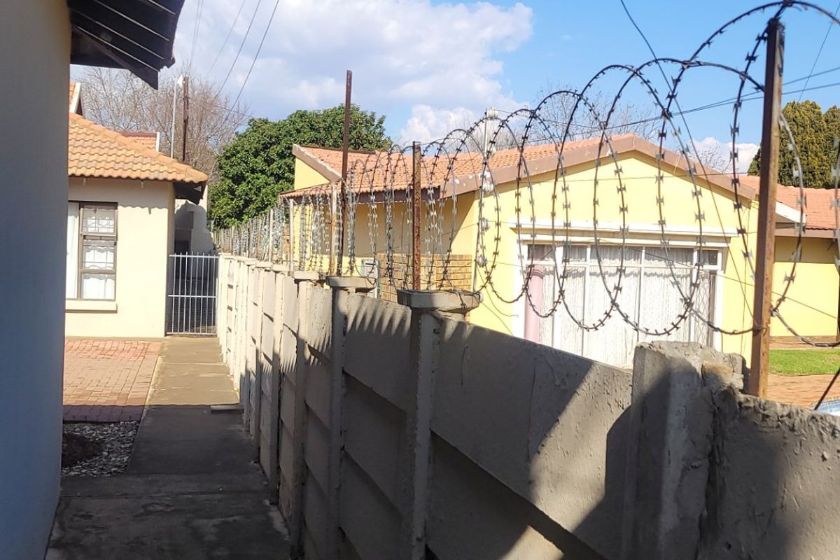 A narrow exterior side passage featuring a precast concrete boundary wall topped with security razor wire and a concrete walkway.