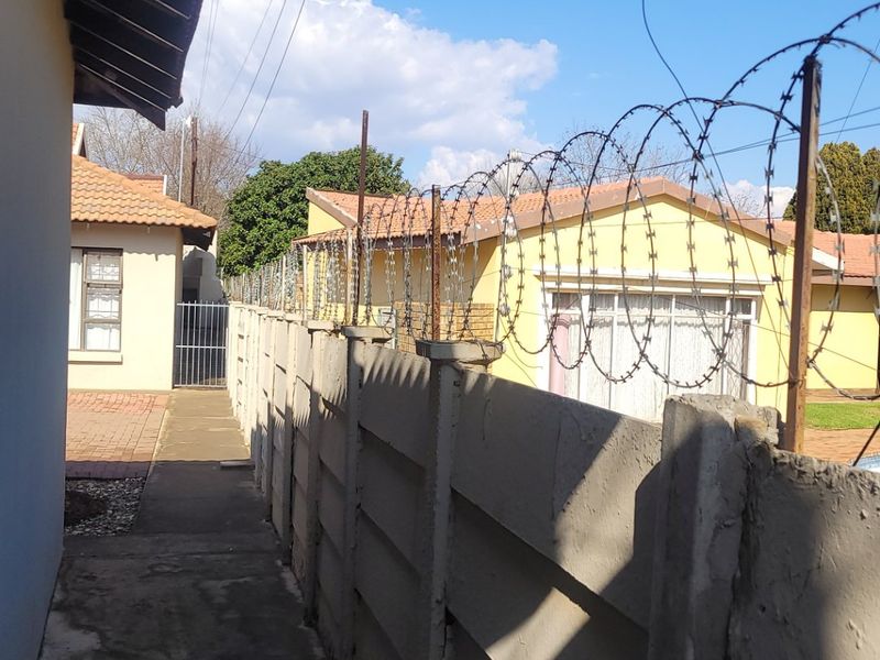A narrow exterior side passage featuring a precast concrete boundary wall topped with security razor wire and a concrete walkway.