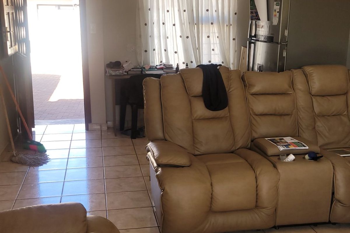 A living room area featuring tiled flooring and recessed downlighting, with direct access to an exterior patio area.