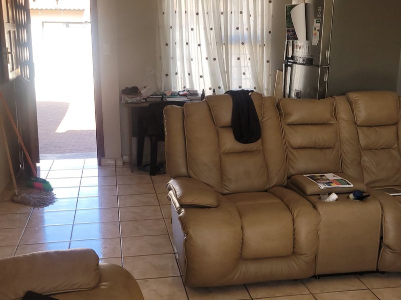 A living room area featuring tiled flooring and recessed downlighting, with direct access to an exterior patio area.