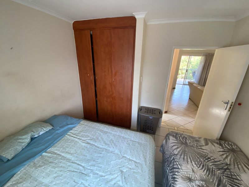 A bedroom featuring built-in wooden wardrobes, tiled flooring, and direct access to an adjacent living area with balcony views.